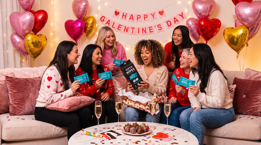Group of female friends laughing while opening funny Galentine's Day gift packages at a party, showcasing novelty gifts and celebration moments 